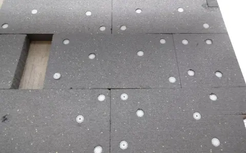 Panneau de polystyrène gris avec des fixations blanches. On compte 3 à 4 chevilles par plaque de polystyrène pour l'isolation.