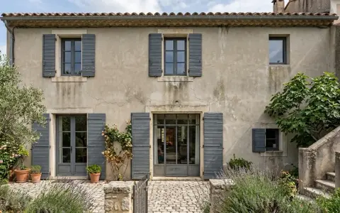 Maison en pierre avec volets gris, idéale pour une aide pour isolation extérieure. Jardin fleuri et pavé devant.