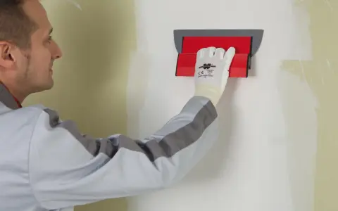 Un ouvrier utilise un outil pour appliquer une bande de placo sur un mur.