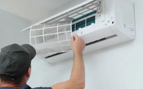 Un homme retire un filtre à air sale d'une unité de climatisation murale, étape essentielle de l'entretien climatisation maison pour un air sain.