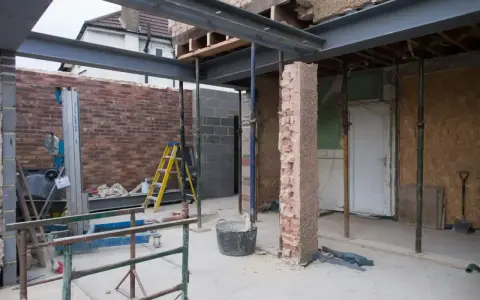 Travaux de rénovation : agrandir ouverture mur porteur avec poutres métalliques. Échafaudages, briques et outils sur le chantier.