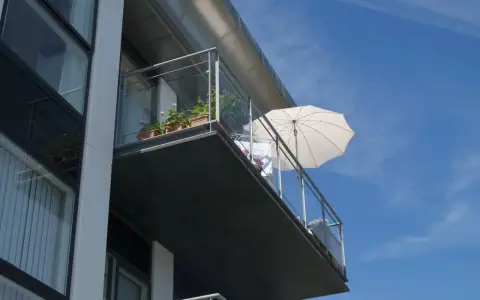 Balcon en béton moderne, prêt pour une rénovation. Des plantes en pot et un parasol blanc attendent le soleil.