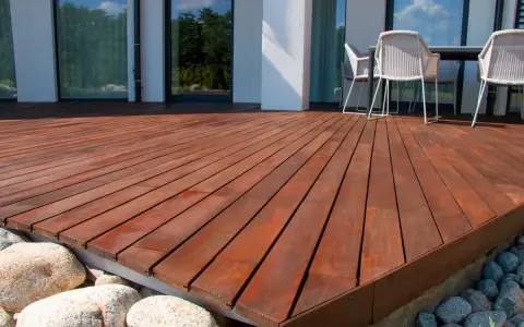 Belle terrasse en bois sur plot, avec des meubles de jardin et des rochers.