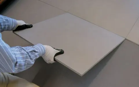 Pose d'une nouvelle dalle pour coller du carrelage sur du carrelage. Les mains gantées ajustent la pièce sur le sol existant.