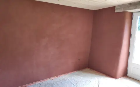 Un coin de pièce aux murs recouverts d'un enduit chaux sable ocre. Le sol est protégé par une bâche. Le plafond est en bois clair.