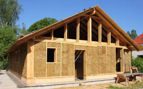 Construction d'une maison en paille écologique, avec une structure en bois visible et des murs isolés en bottes de paille.
