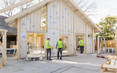 Construction d'une maison écologique passive en bois. Des ouvriers en gilets de sécurité supervisent le chantier.