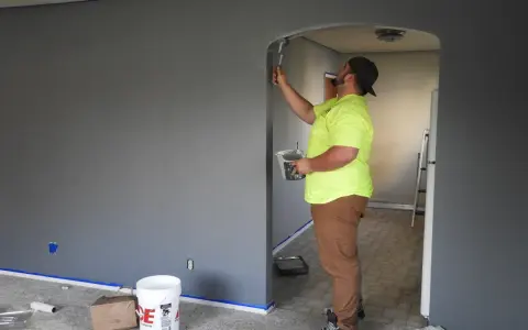 Un peintre en bâtiment applique de la peinture sur un mur. Pour savoir comment reconnaître un mur porteur, observez la structure et l'épaisseur.