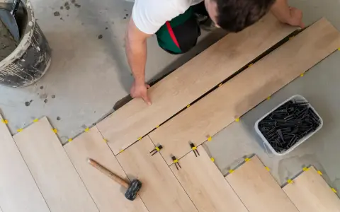 Pose d'un carrelage imitation bois sur un plancher. Un ouvrier pose les lames, des cales jaunes et noires assurent l'espacement.