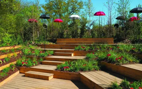 Un jardin aménagé avec des terrasses en bois et une **profondeur marche escalier extérieur** sur plusieurs niveaux, décoré de tulipes rouges et de parasols colorés.