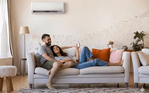 Couple détendu sur un canapé, profitant du confort d'une climatisation réversible. Aide EDF pour un intérieur agréable.