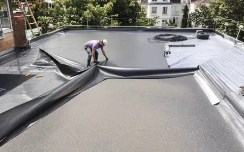 Un ouvrier pose une membrane pour l'étanchéité d'une terrasse en béton. Le travail est en cours.