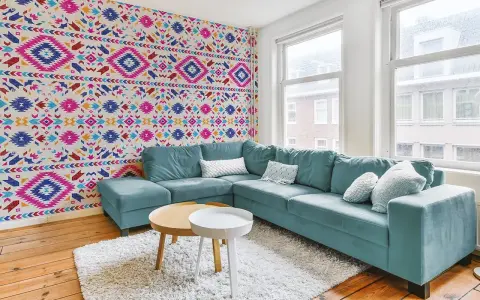 Un salon moderne avec un canapé bleu sarcelle et un papier peint intissé aux motifs ethniques colorés.
