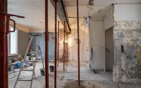 Chantier en cours : étais rouges soutenant un linteau, murs abattus, échelle et matériaux. Préparation pour une ouverture mur porteur.
