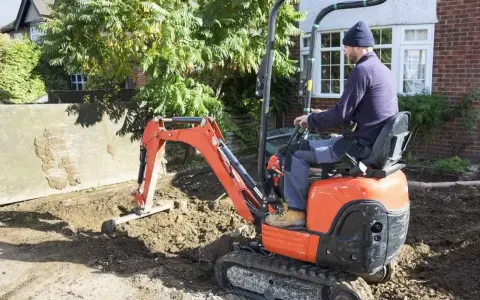 Un ouvrier manœuvre une mini-pelle orange pour des travaux de terrassement. Le prix du terrassement au m2 est une préoccupation pour ce chantier.