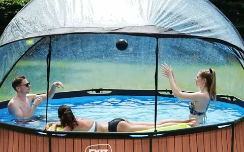 Trois personnes jouent dans une piscine hors sol sous un abri transparent. Idéal pour savoir comment fabriquer un abri piscine hors sol.