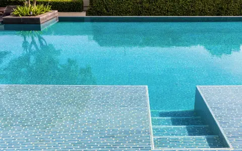 Élégante rénovation piscine mosaïque bleue, avec des marches carrelées et une végétation luxuriante.