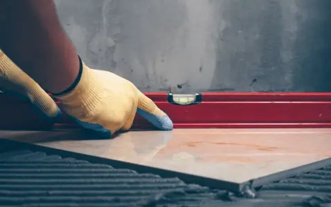 Pose d'un carrelage avec un niveau à bulle pour vérifier l'épaisseur du carrelage et de la colle.