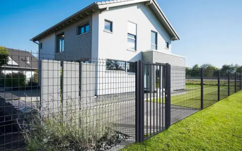 Une clôture privative en limite de propriété délimite un jardin moderne avec une maison blanche et un portillon.