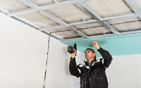 Un ouvrier réalise le schema montage placo plafond, fixant une plaque verte sur une structure métallique.