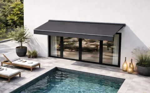 Un store banne gris protège une terrasse moderne avec piscine. L'entretien de ce store est essentiel pour profiter de cet espace de détente.