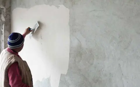 Un artisan applique un enduit chaux sable intérieur sur un mur avec une truelle. La texture naturelle du mortier est visible.