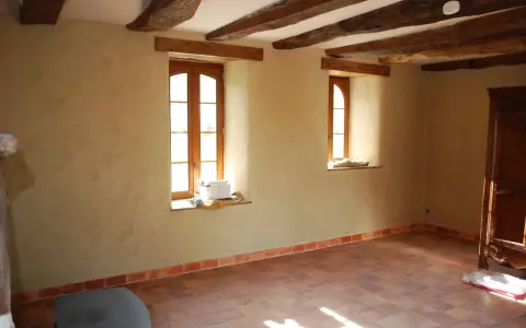 Intérieur d'une pièce aux poutres apparentes, murs en chaux chanvre pour une isolation naturelle, sol carrelé.