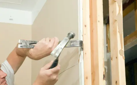 Main tenant utilise un pied-de-biche et un marteau pour démonter une cloison placo. Le travail progresse bien.