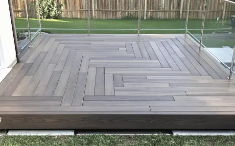Une belle pose terrasse bois sur terre, avec un motif en chevrons moderne et des garde-corps en verre.