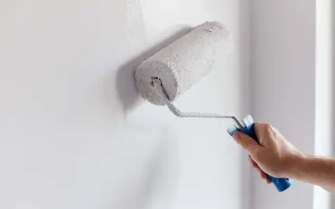 Main d'homme appliquant de la peinture blanche sur un mur avec un rouleau. Un guide visuel pour comment peindre un mur.