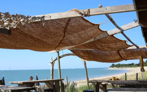 Installation d'une voile d'ombrage en toile de jute sur une structure en bois, offrant une vue sur la mer et la plage.