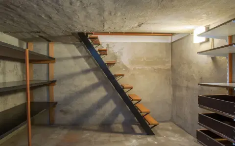 Escaliers métalliques menant à une cave en cours d'aménagement, avec étagères brutes et murs en béton. Idéal pour creuser une cave sous sa maison.