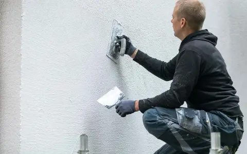Un ouvrier applique un enduit sur un mur extérieur avec une truelle.