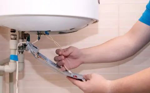 Main tenant vérifie son chauffe eau qui fait disjoncter. Il tient une pièce détachée avec des fils électriques.