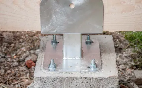 Pied de poteau métallique fixé sur un plot béton à enterrer, soutenant une poutre en bois.