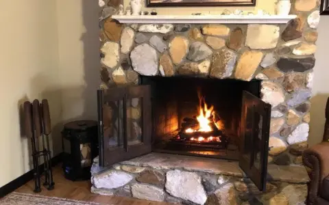Un feu crépite dans une cheminée en pierres. Quel parement derrière poêle à bois, avec des accessoires de cheminée à gauche.