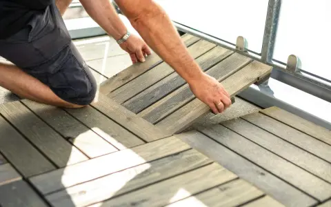 Un homme installe des dalles de terrasse en bois sur son balcon. Une belle idée sol balcon pour un espace extérieur accueillant.