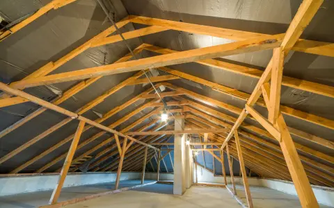 Charpente de grenier en bois, avec une bâche noire recouvrant le toit, suggérant une isolation rampant par l'intérieur en cours.