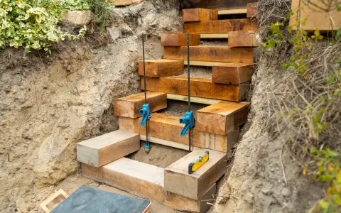 Construction d'un escalier traverse bois et gravier. Des poutres de bois sont empilées pour former des marches dans une tranchée.