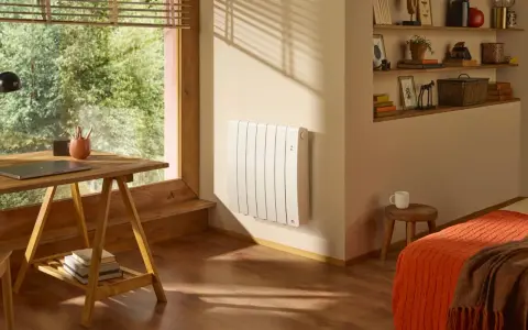 Radiateur blanc mural, discret et efficace, diffusant une chaleur douce grâce à son fluide caloporteur. Un coin bureau et un lit douillet complètent cette pièce chaleureuse.