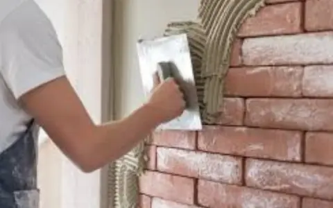 Un ouvrier applique de l'enduit sur une brique avec une truelle, créant une texture rustique.