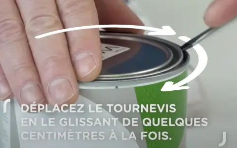 Main tenant un tournevis, on montre comment ouvrir un pot de peinture en faisant levier sur le couvercle.