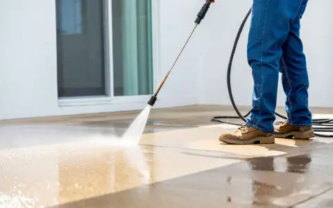 Un homme nettoie sa terrasse carrelage avec un nettoyeur haute pression. L'eau projetée fait briller le sol.