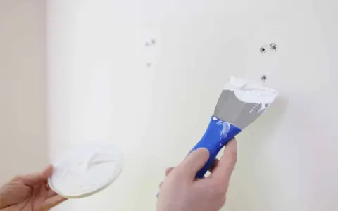 Main tenant en main une spatule chargée de mastic, prêt à reboucher trou mur.