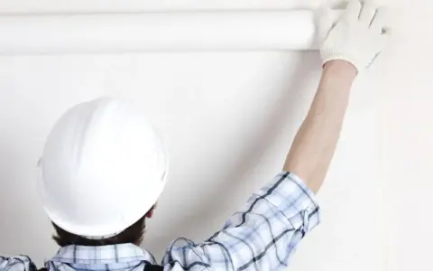 Un ouvrier en casque blanc déroule une **pose toile de verre** sur un mur blanc.
