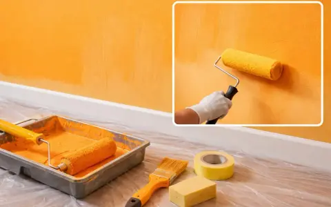Un rouleau de peinture jaune crée des traces de rouleau à la lumière sur un mur orange. Matériel de peinture à proximité.