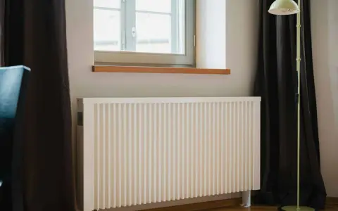 Radiateur électrique blanc moderne près d'une fenêtre. Idéal pour bénéficier de l'aide de l'état pour changer radiateur électrique.
