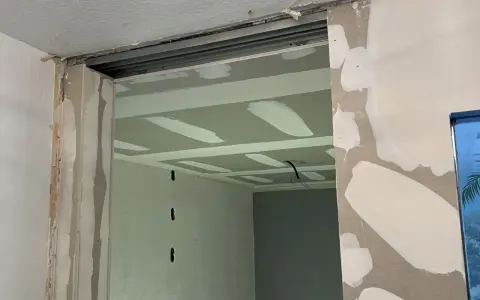 Ouverture dans un mur en cours de travaux de rénovation, avec plaques de plâtre et rails apparents.