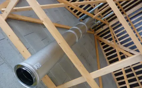 Installation d'un tubage cheminée en métal dans une charpente en bois. Le conduit traverse un mur en parpaings.