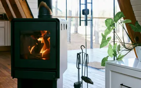 Un poêle à bois MCZ crépitant dans un chalet moderne, avec une grande baie vitrée donnant sur la forêt. Un avis positif s'impose pour ce coin cosy.